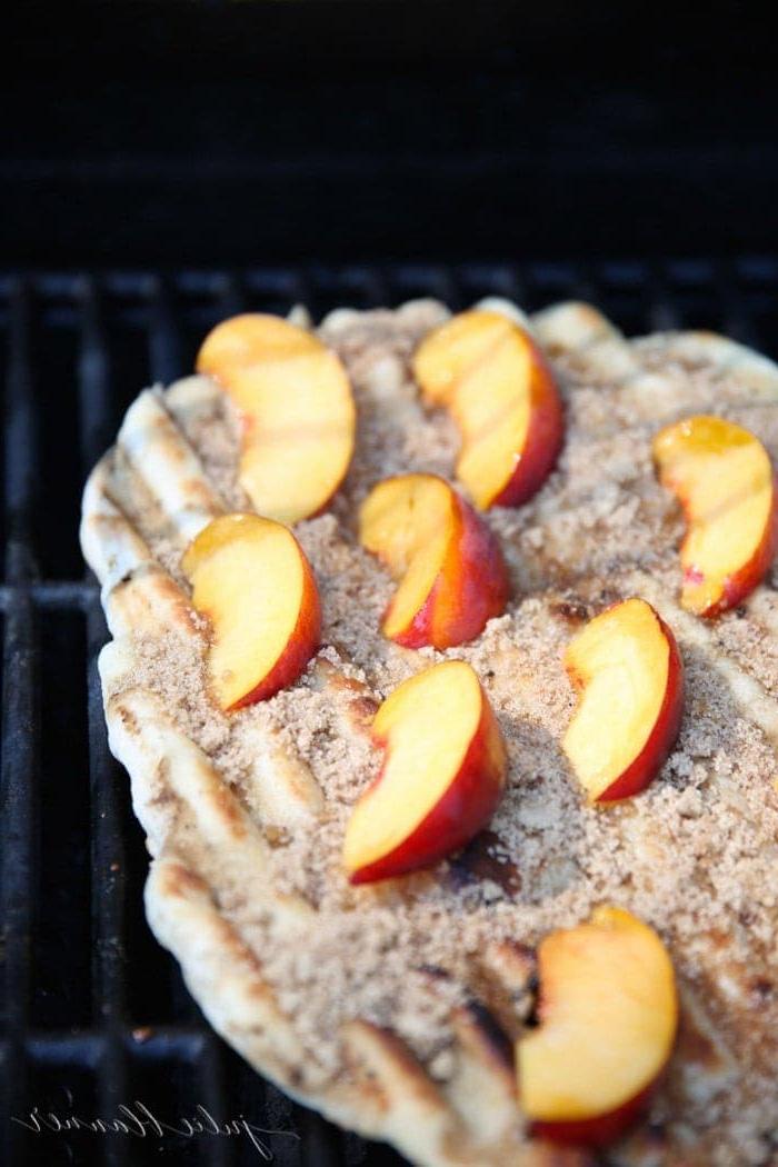 Pizzateig auf einem Außengrill ausgebreitet, belegt mit geschnittenen Pfirsichen, Zimt und braunem Zucker