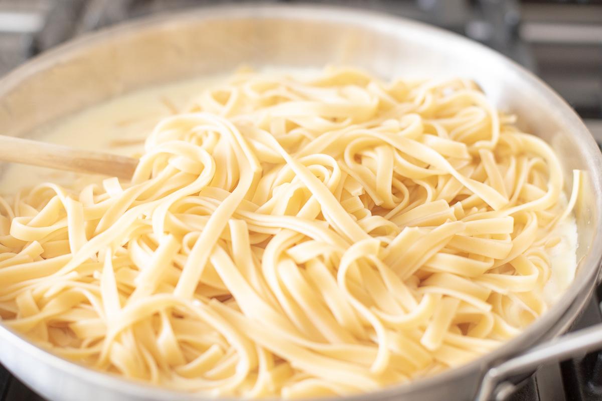 Wie man Nudeln aufwärmt 9 Ein Edelstahlkochtopf auf einem Herd, gefüllt mit Pasta. Das Bild ist Teil eines Tutorials zum Aufwärmen von Pasta.