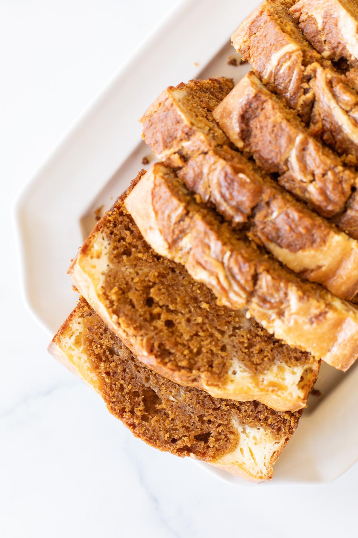 Ein wunderschön gebackener Laib Kürbis-Käsekuchen-Brot, liebevoll auf einer weißen Platte angerichtet, die seine goldene Farbe und Textur hervorhebt.