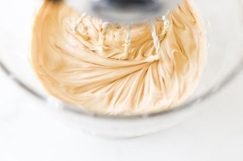 Nahaufnahme von cremiger Erdnussbutter, die in einer Glasschüssel mit einem Standmixer gemischt wird.
