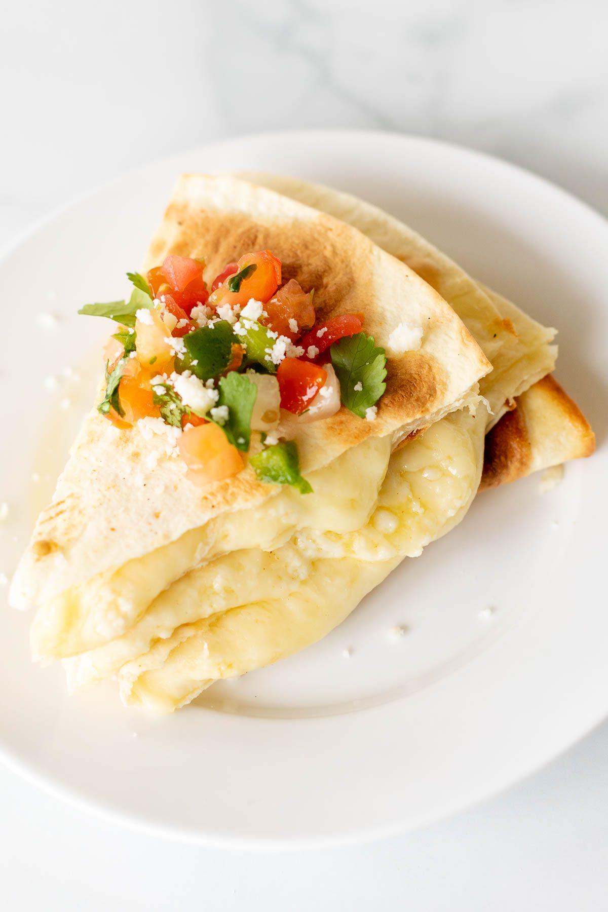 Käsequesadillas 9 In Scheiben geschnittene und gestapelte Käse-Quesadilla auf einem weißen Teller, mit Pico de Gallo belegt
