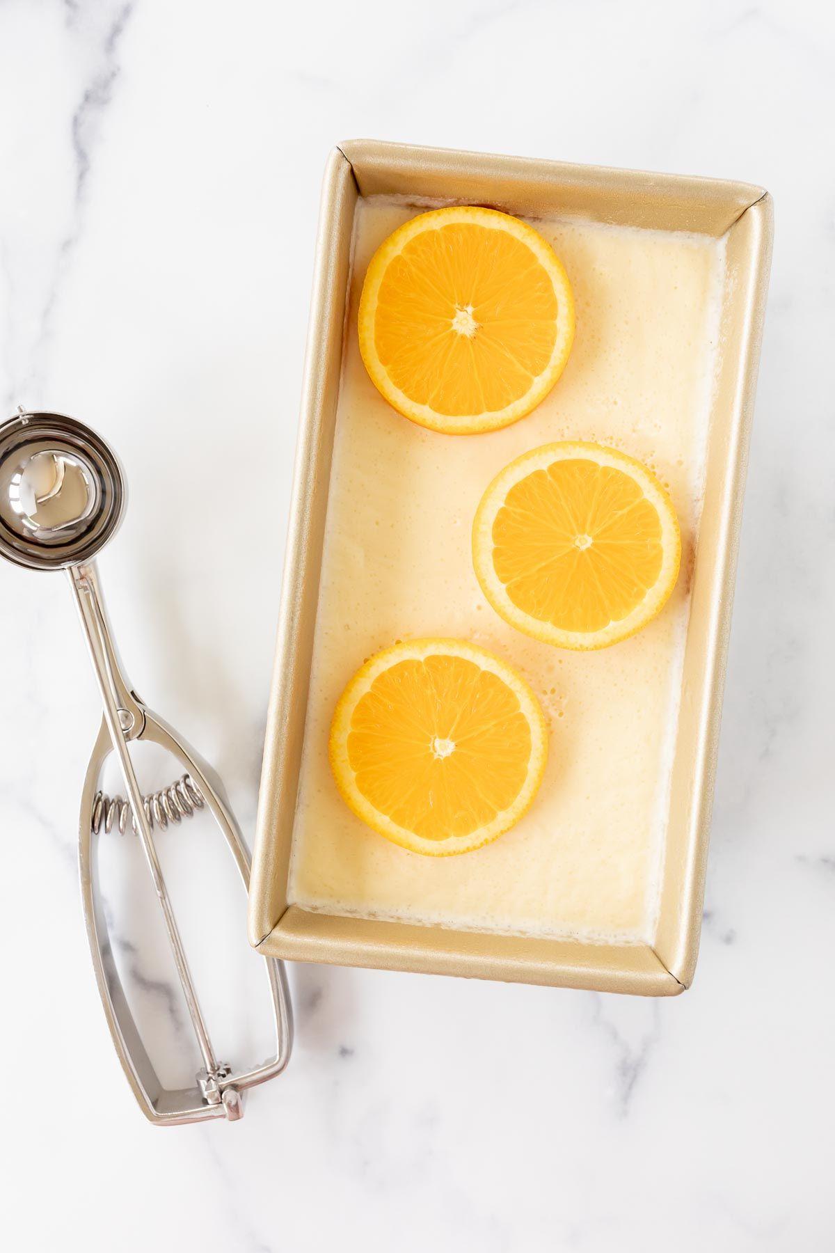 Hausgemachtes Orangen-Sherbet in einer goldenen Brotkastenform, mit einem Eisportionierer bereit zum Servieren