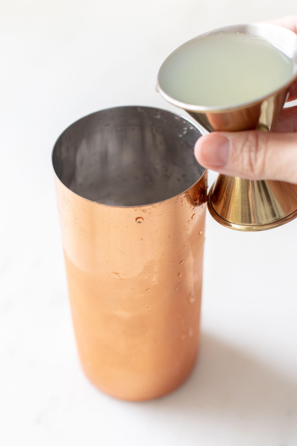 Ein kupferfarbener Shaker mit einer Hand, die Cadillac Margarita Zutaten mixt.
