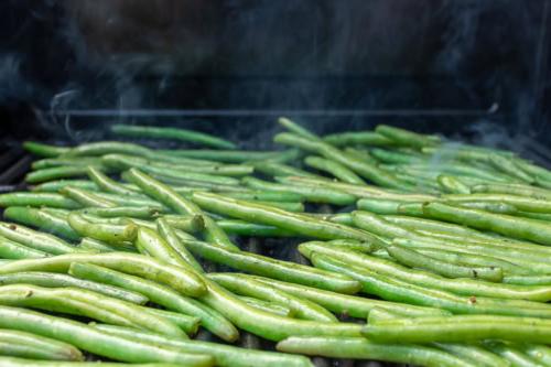 Eine große Menge gegrillter grüner Bohnen brutzelt auf dem Grill, sichtbarer Dampf steigt auf.