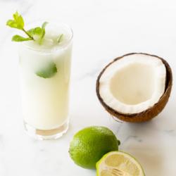 Kokosnuss-Mojito 10 Ein Kokos-Mojito, garniert mit Minze, auf einer Marmorfläche. Limetten und eine offene Kokosnuss daneben.