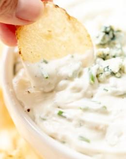 Ein Blauschimmelkäse-Dip in einer weißen Schale, mit einer Hand, die einen Chip zum Eintauchen hält – ein köstlicher Snack.