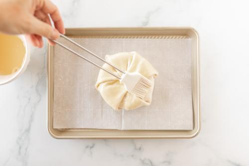 Eistreiche wird über ungebackenen Brie en Croute auf Backpapier bestrichen – Für den unwiderstehlichen Bäckerei-Glanz