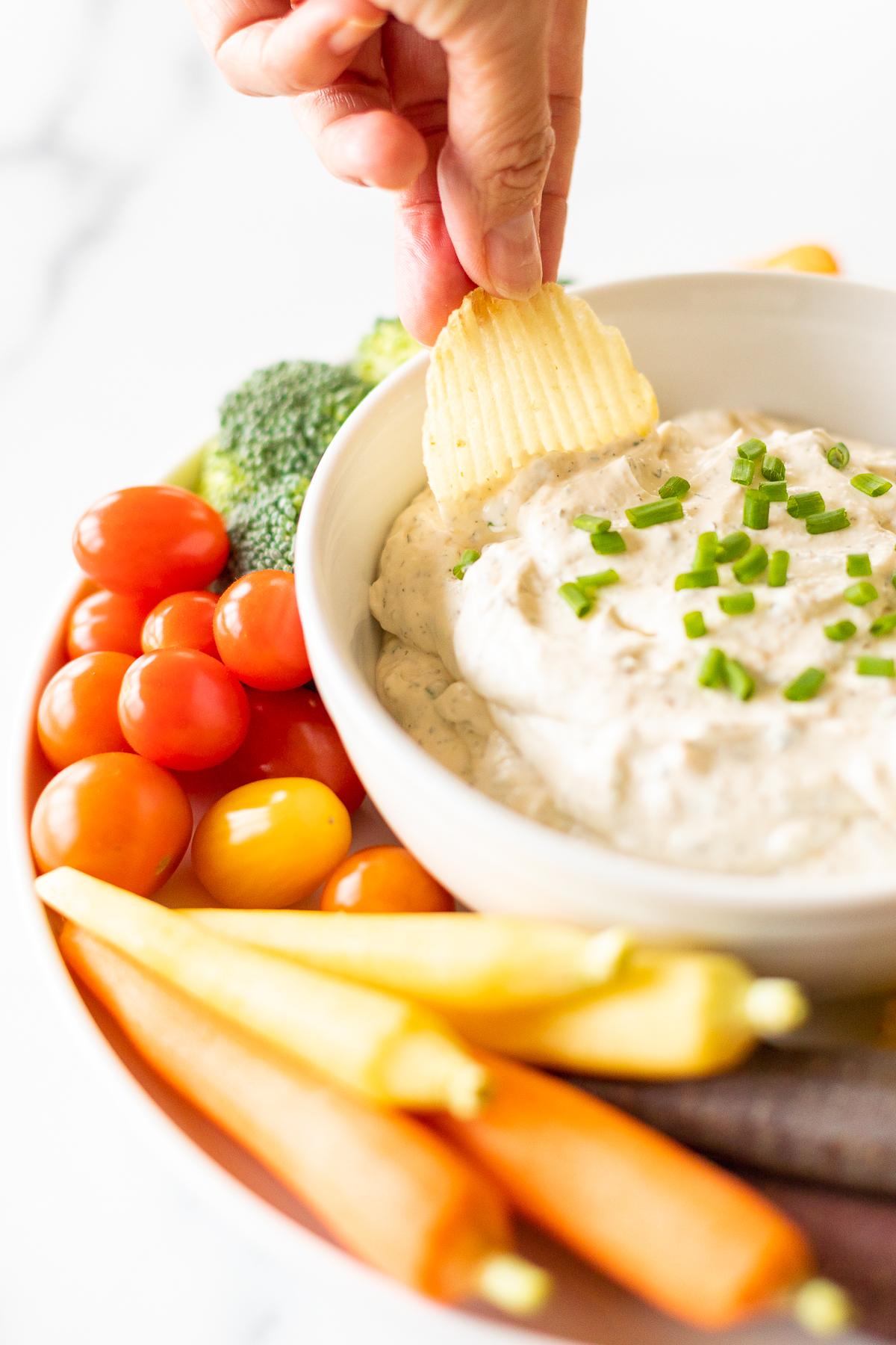 Ranch-Dip 10 Eine gerillte Kartoffelchips wird in einen Ranch Dip getaucht, der auf einer Servierplatte mit Gemüse steht.