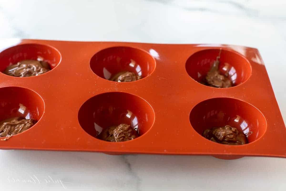 Eine rote Silikonkugelform, gefüllt mit Schokolade für mexikanische Trinkschokolade Bomben.