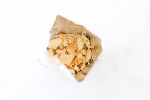 Offener Snackbeutel mit zerbröselten Stücken auf weißem Hintergrund.