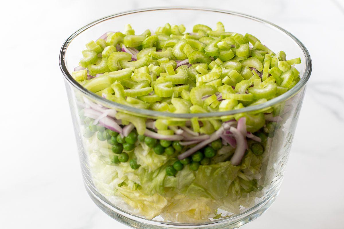 Gehackter Salat mit Erbsen, Zwiebeln und Sellerie in einer Glasschale.