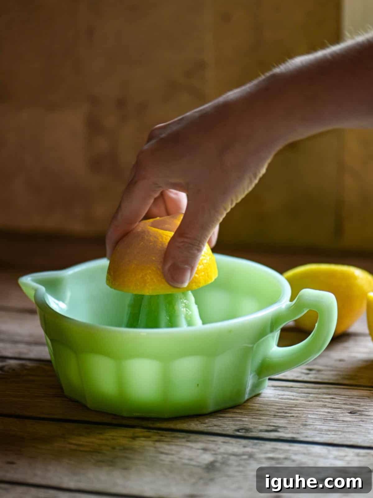 Signature Lavender Lemonade 5 A hand squeezing a lemon over a green juicer.