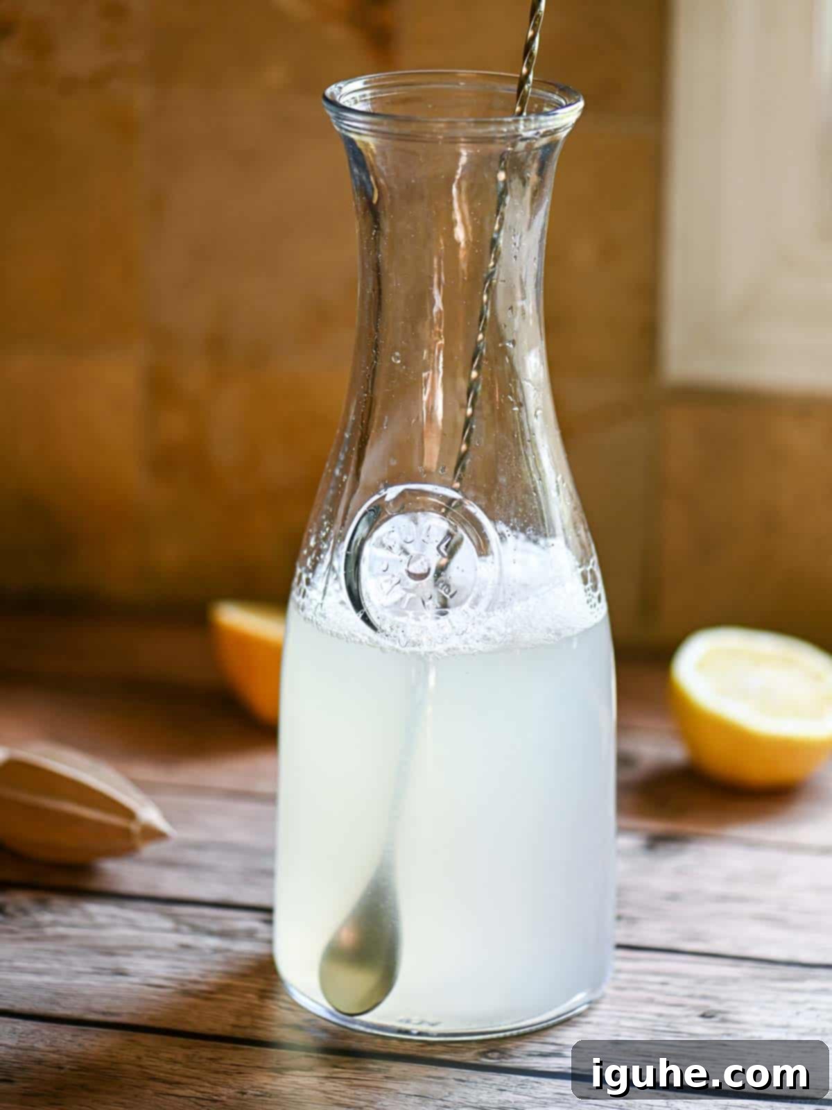 Signature Lavender Lemonade 9 A pitcher with a spoon and lemon slices on a wooden table.