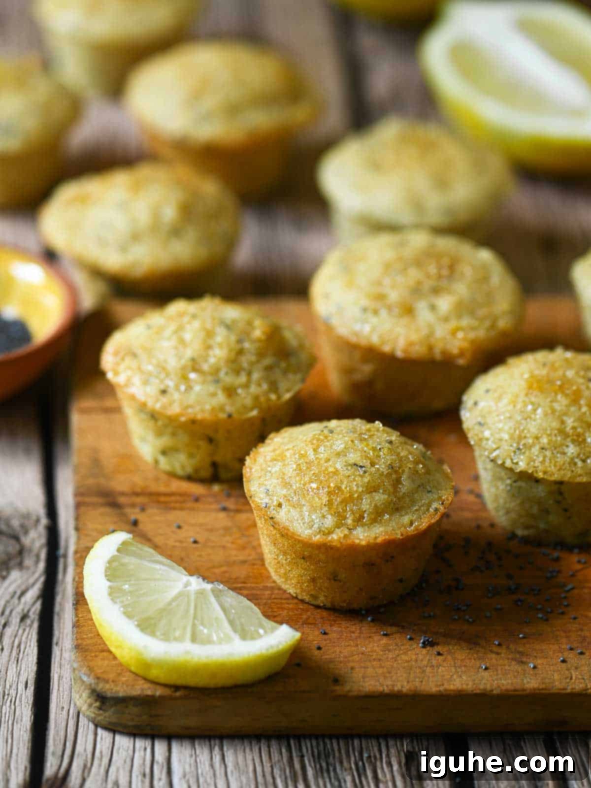 Zesty Lemon Poppy Seed Gems 2 Delicate mini lemon poppy seed muffins elegantly arranged on a rustic wood board, with a vibrant lemon wedge adding a pop of color and a fresh, inviting feel.