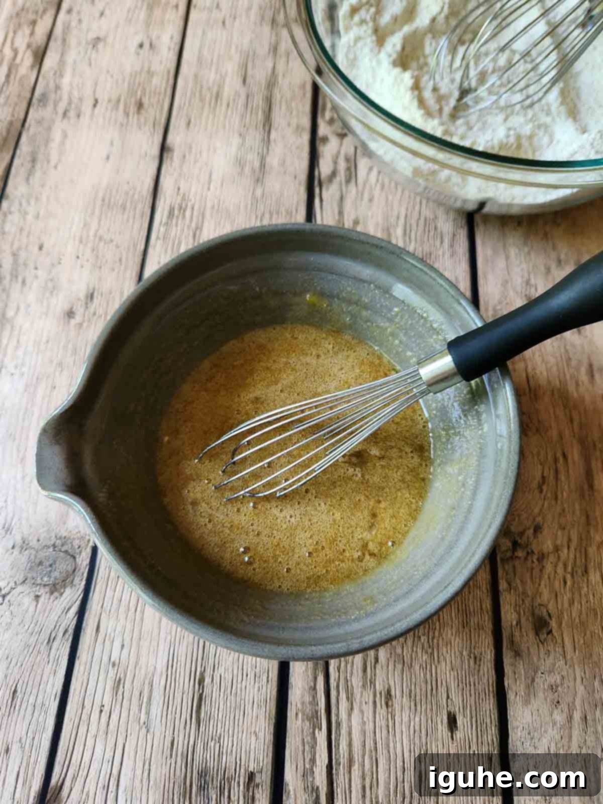 Zesty Lemon Poppy Seed Gems 3 A whisk swirls liquid ingredients in a mixing bowl, creating a smooth, golden batter for the mini lemon poppy seed muffins.