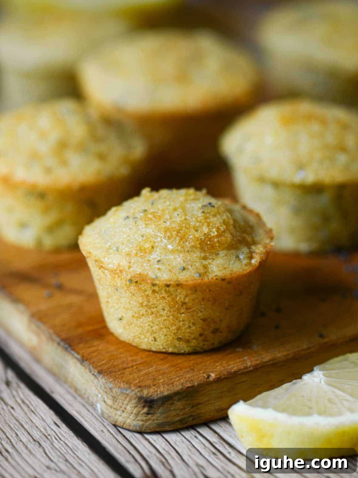 Zesty Lemon Poppy Seed Gems 7 A delectable close-up of a perfectly baked mini lemon poppy seed muffin, showcasing its golden-brown top and tender crumb, resting on a rustic wood board.