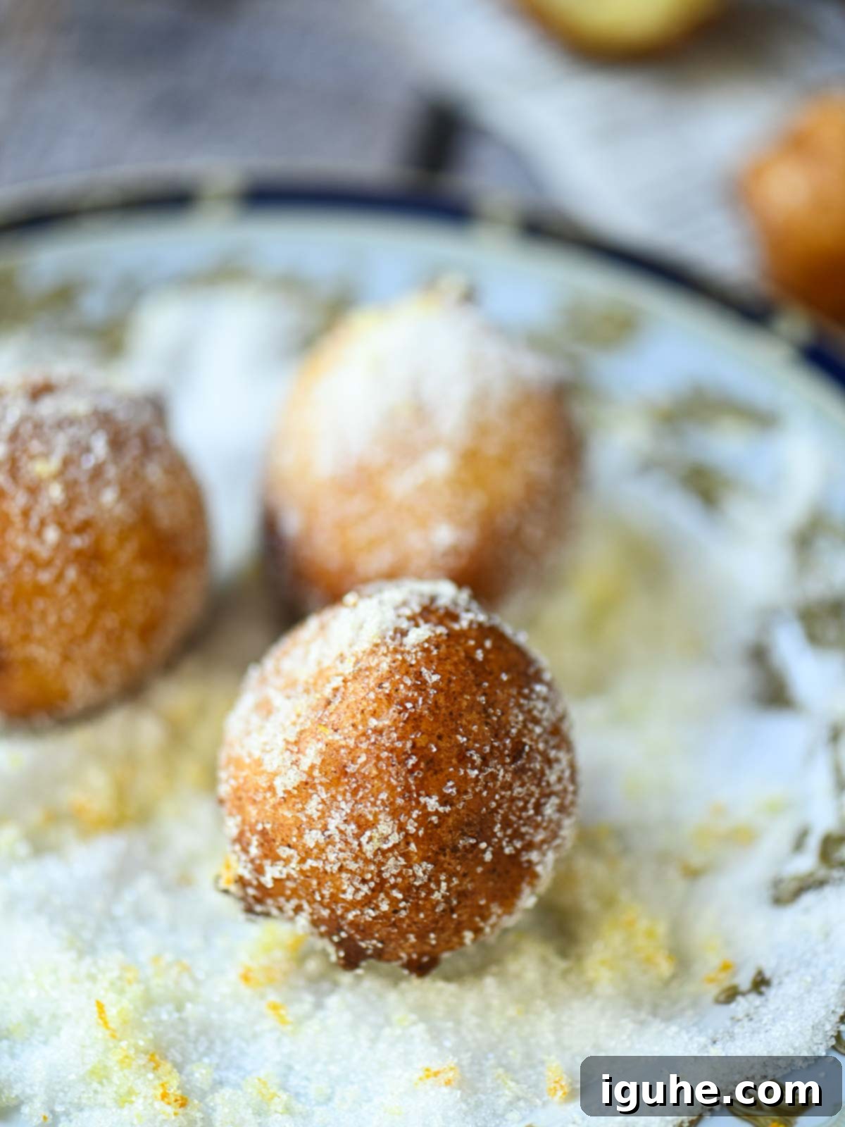 Italian Orange Ricotta Doughnuts 4 Donut being rolled in a plate of orange sugar.