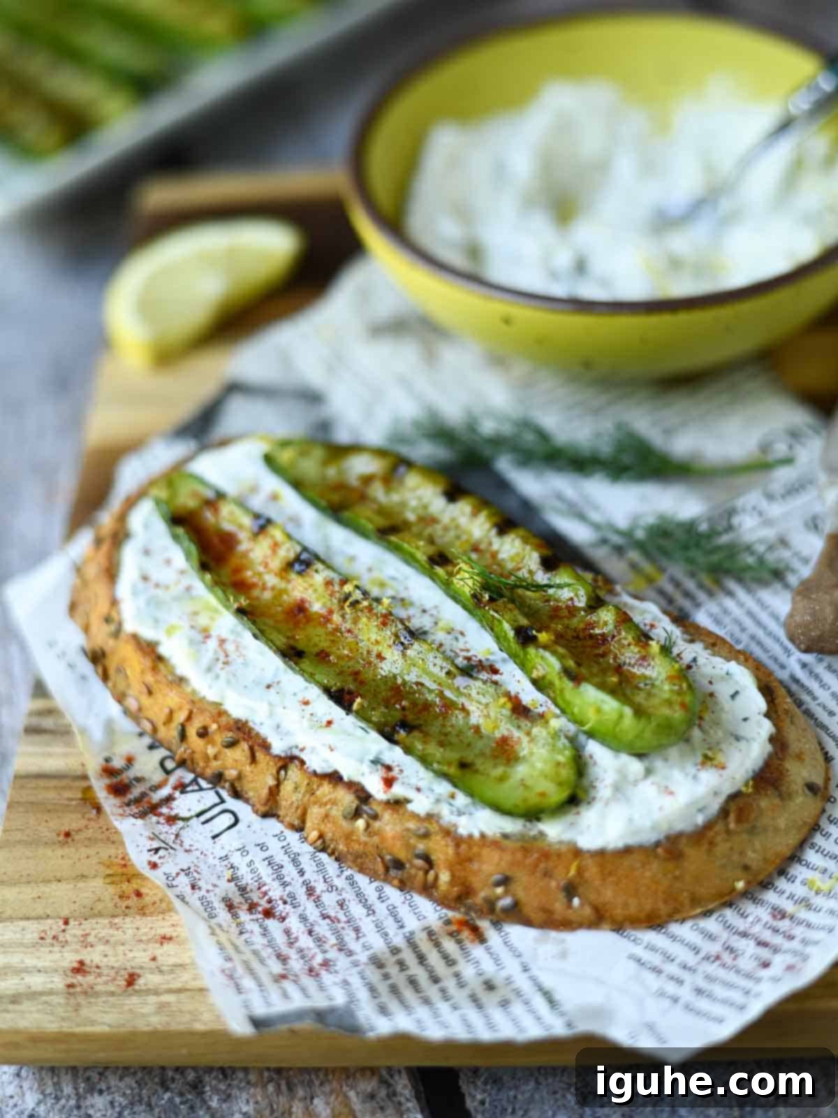 Crispy toast topped with creamy tzatziki and smoky grilled cucumber slices, garnished with fresh dill on a rustic wooden board.