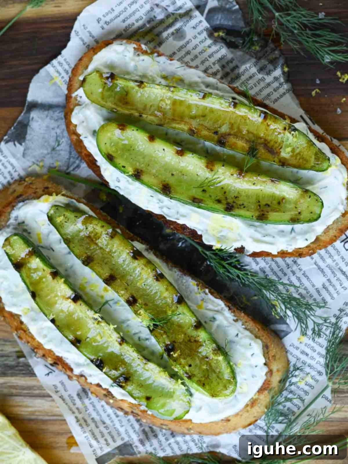 Smoky Grilled Cucumber & Tangy Tzatziki Toast 6 Overhead shot of two Tzatziki toasts with grilled cucumbers and fresh dill on a wooden cutting board.