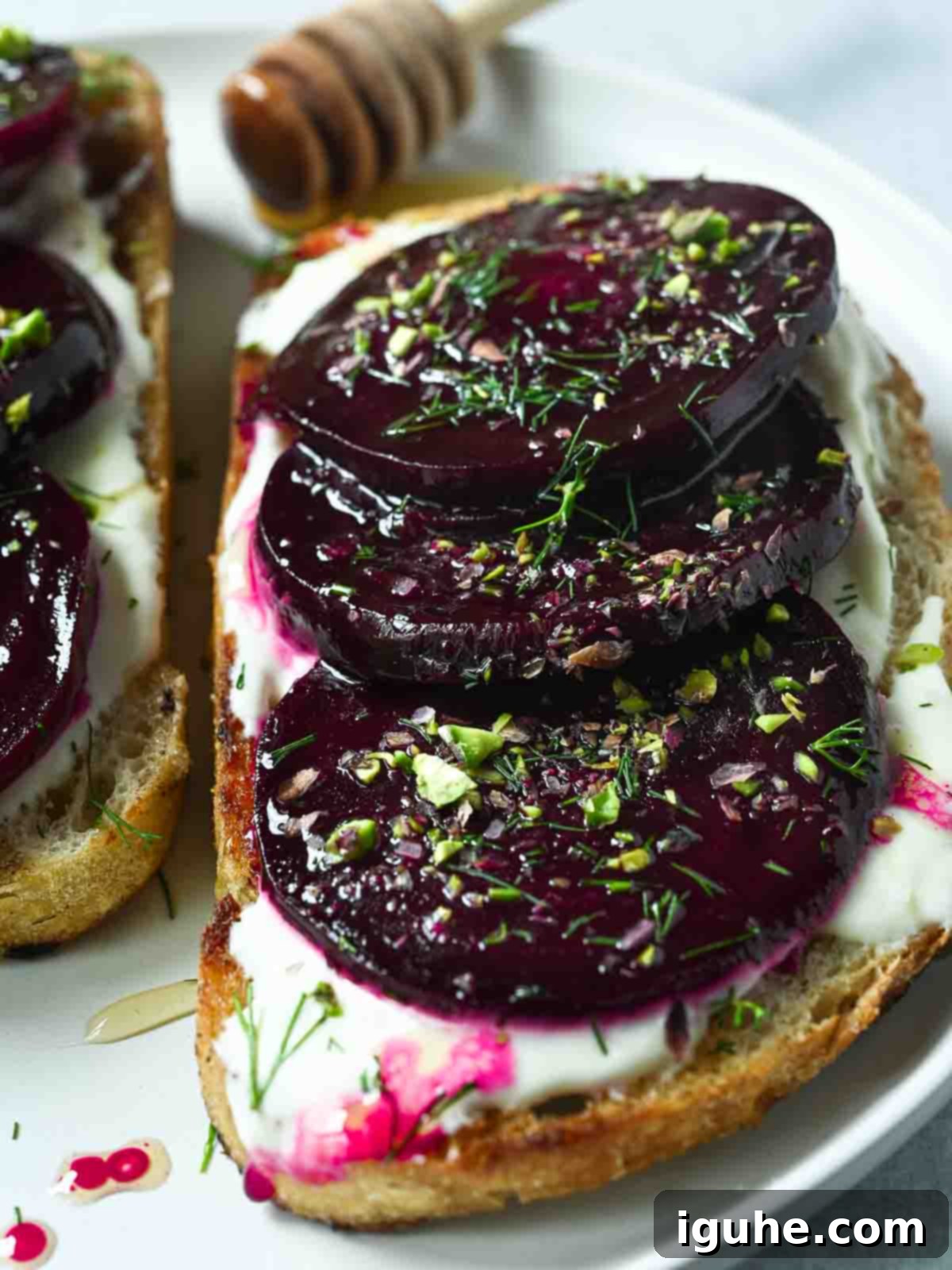 Crimson Beet Toast with Herbed Creme Fraiche 7 Close-up of perfectly sliced beets arranged on toast with creamy spread on a white plate.