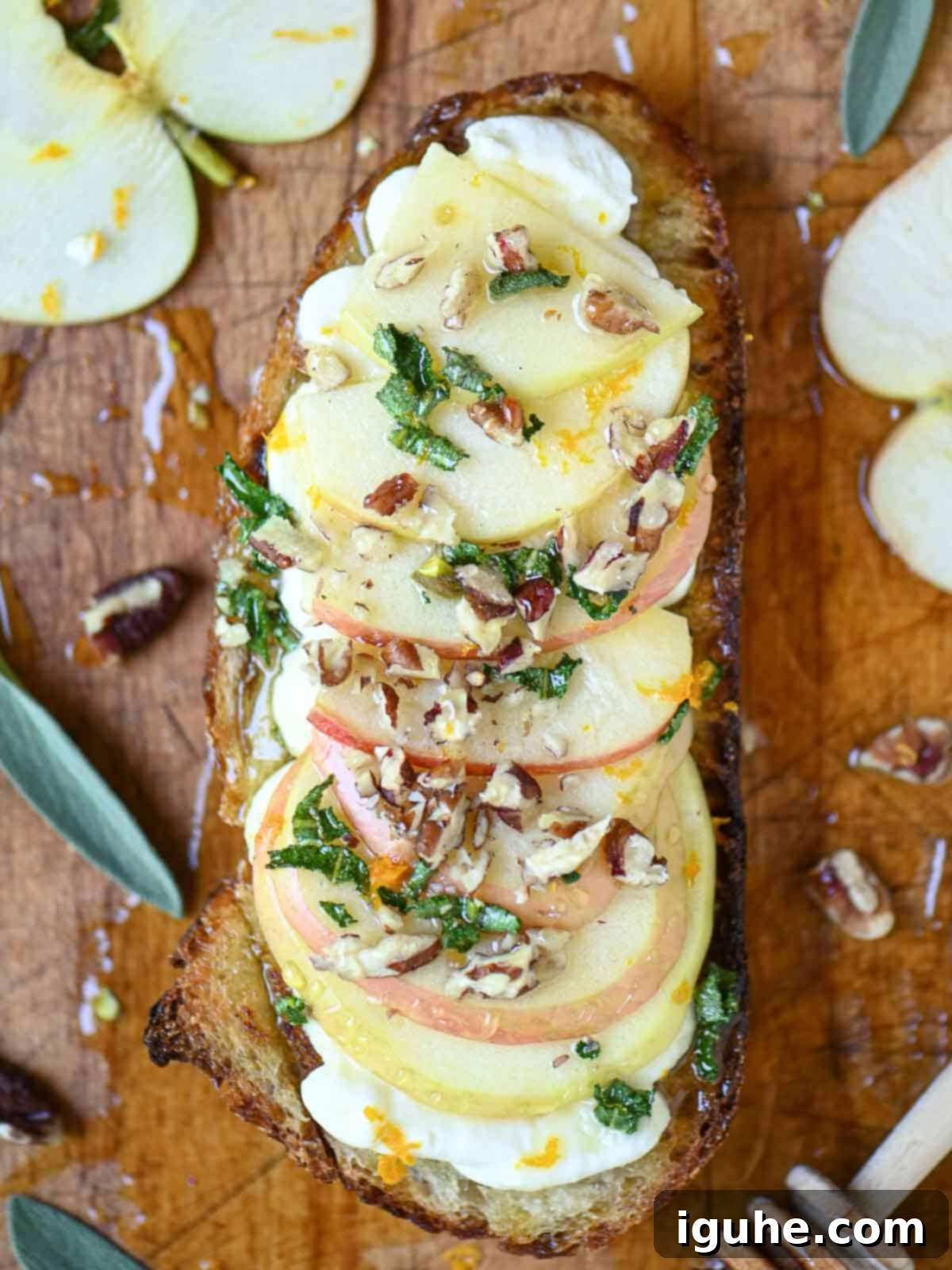 Overhead of apple toast with sage honey on a cutting board, garnished with fresh sage leaves.