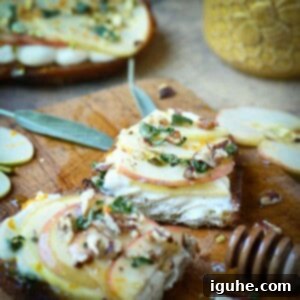 Creamy Ricotta Apple Toast with Sage-Kissed Honey 9 Apple toast sliced open on a cutting board, garnished with fresh sage leaves and a honey drizzle.