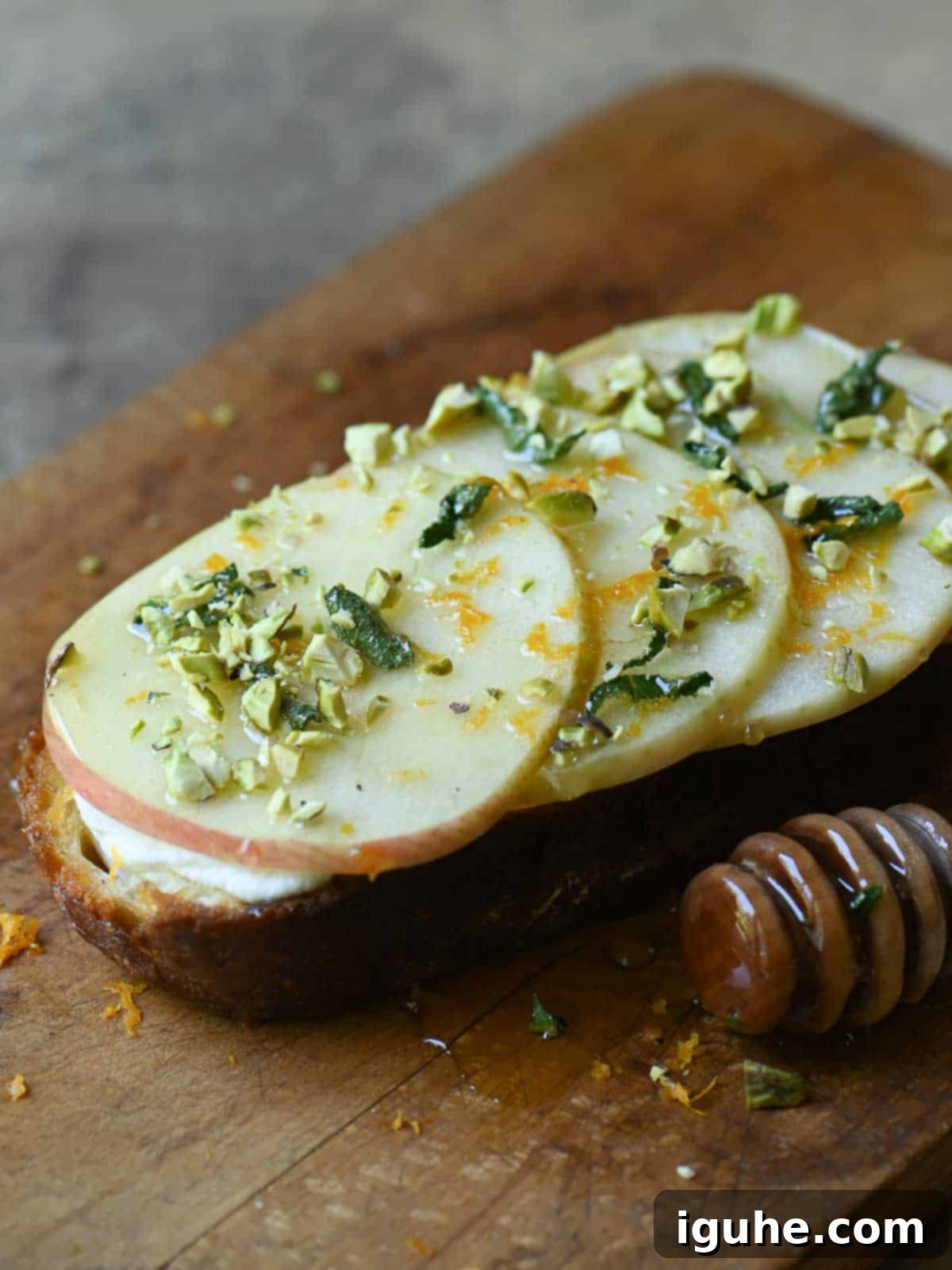 Creamy Ricotta Apple Toast with Sage-Kissed Honey 7 Finished apple toast with ricotta, sage honey, orange zest, and chopped nuts on a cutting board.