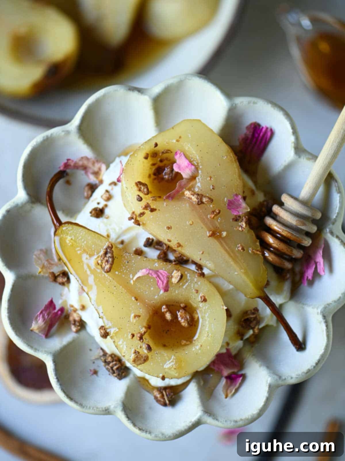 Overhead of poached pears in a flower plate with rose petals on top.