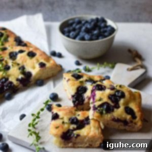 Sweet and Savory Blueberry Thyme Focaccia 8 Angled view of blueberry and thyme focaccia on a serving grey serving board with blueberries in the background.