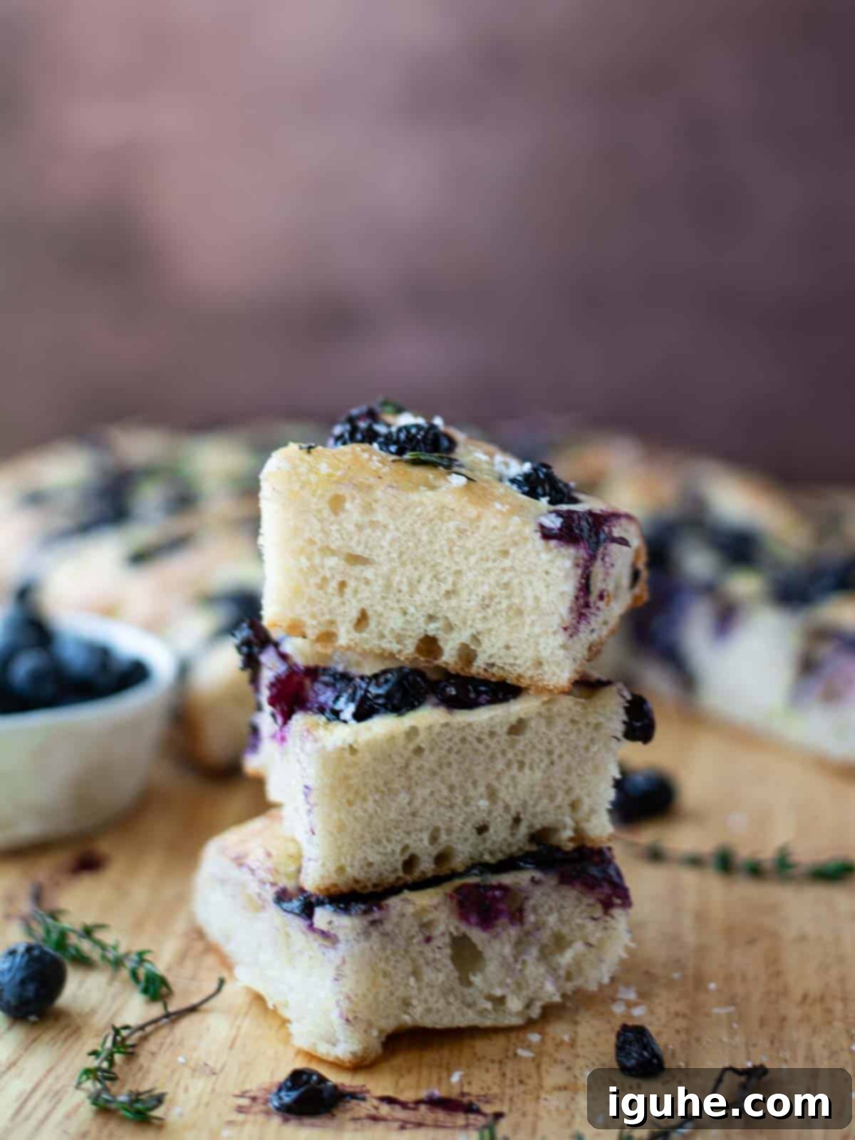 Sweet and Savory Blueberry Thyme Focaccia 6 Three slices of focaccia piled on top on each other on a wooden board.