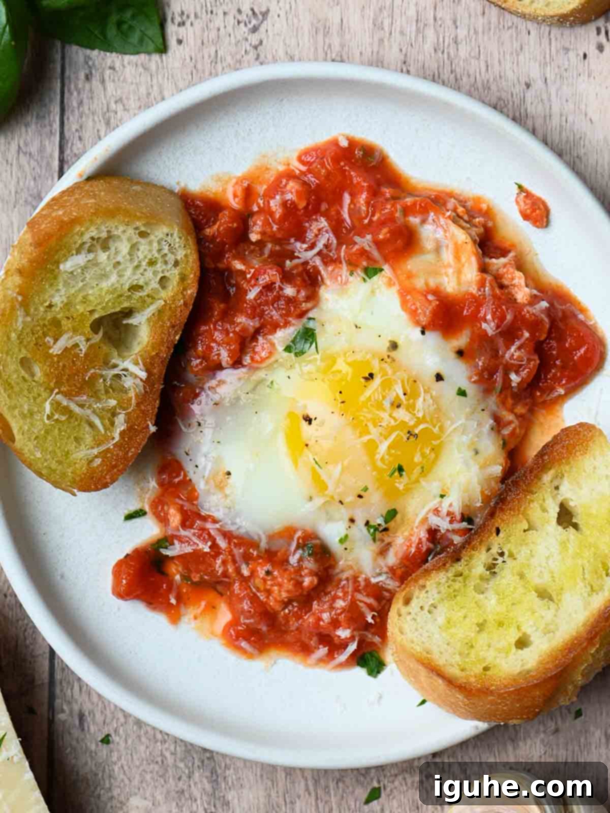 Domates Alevinde Yumurtalar 11 Overview of Eggs in Purgatory, with a portion of sauce, egg, and bread on a white plate.