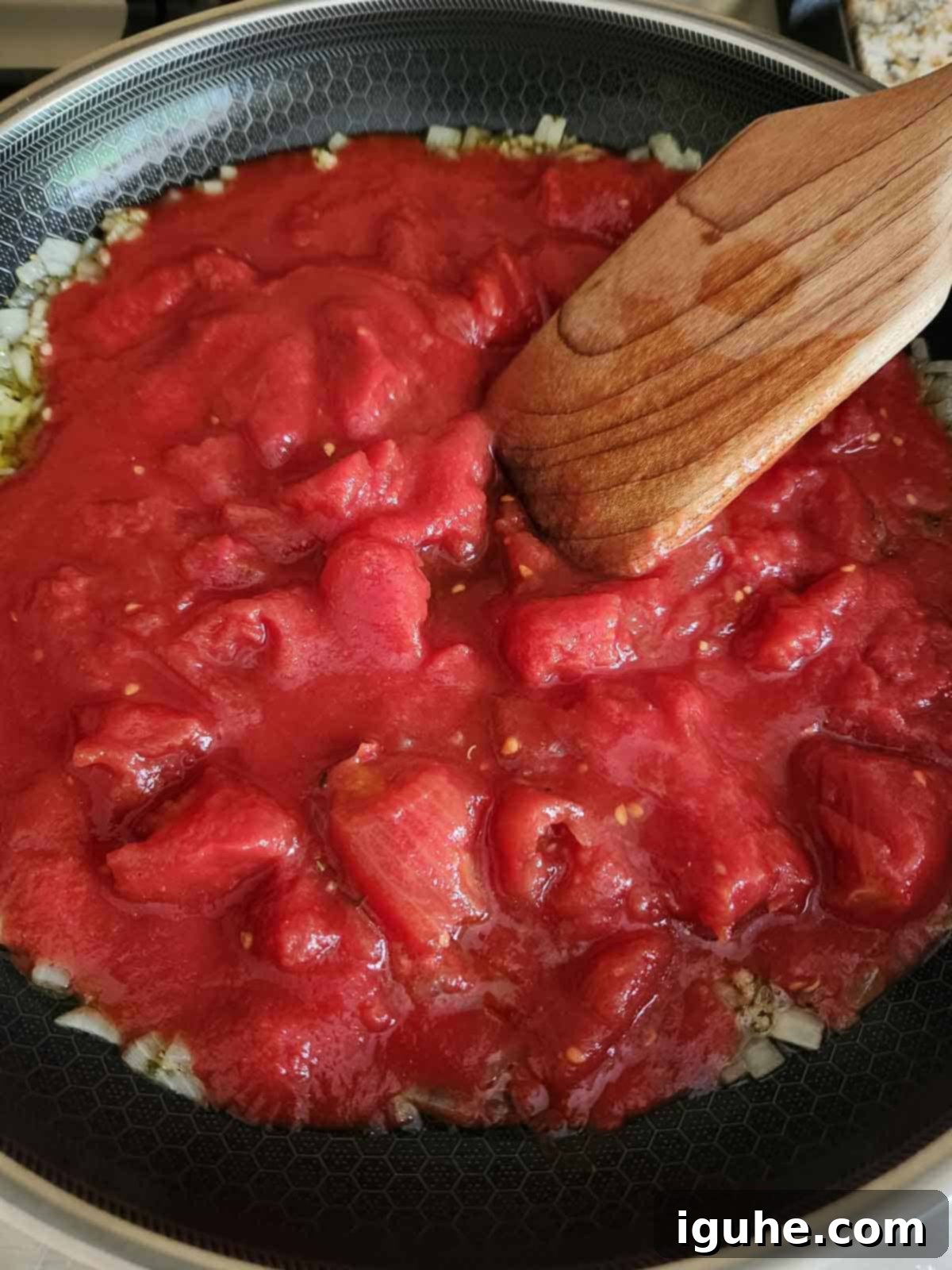 Domates Alevinde Yumurtalar 5 Step 2: Adding canned whole tomatoes to the sautéed onions and garlic, then crushing them with a spoon.