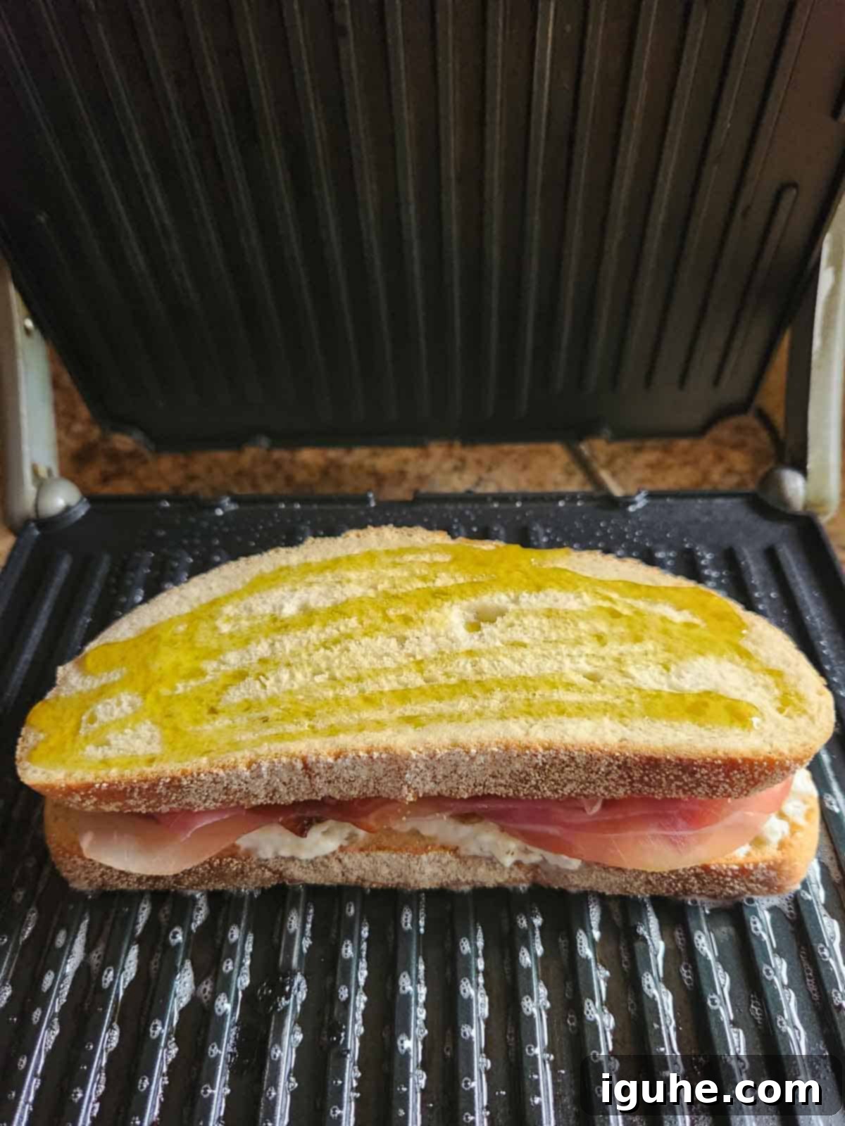 Sweet and Savory Peach Prosciutto Burrata Panini 5 A peach panini being pressed on an electric panini maker, showing grill marks forming.