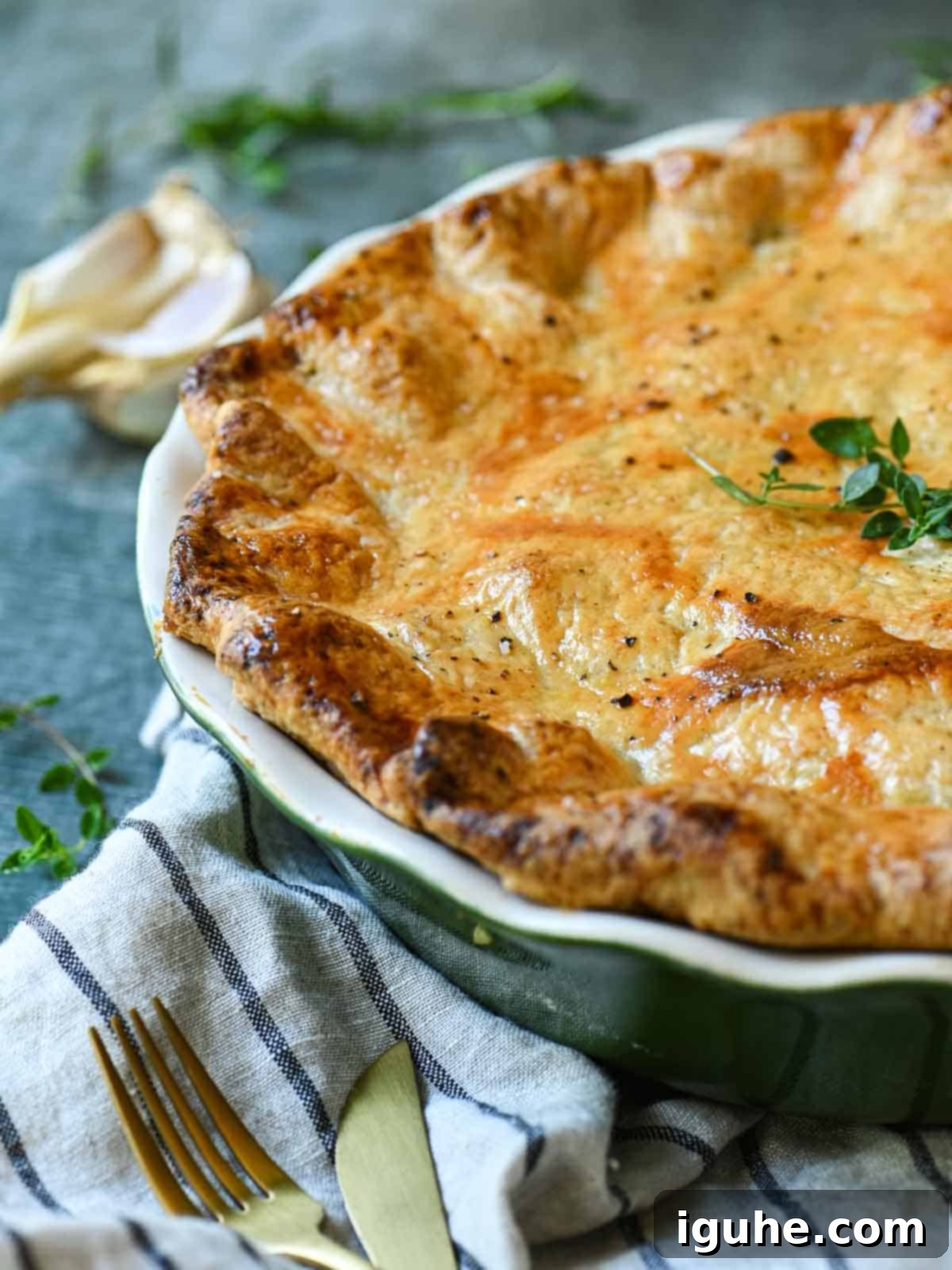 Close-up of chicken pot pie showing the golden, flaky crust with fresh herbs next to it.