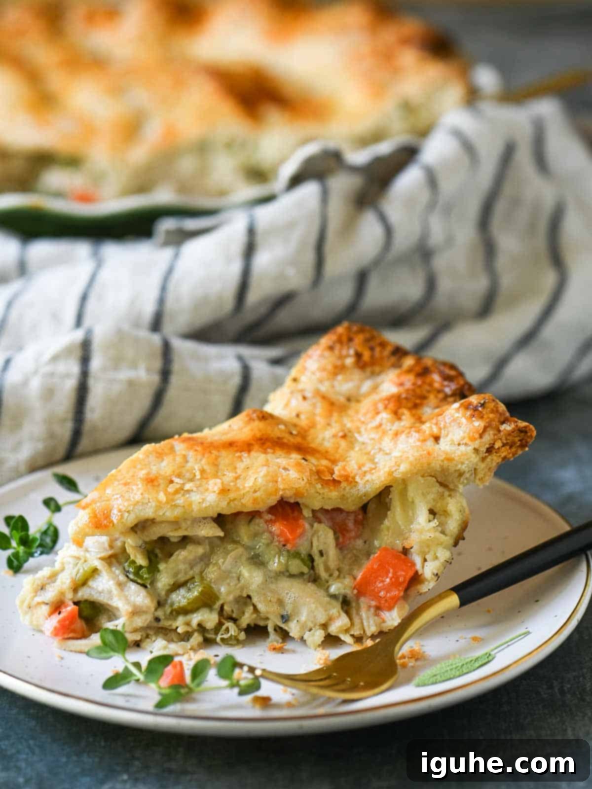 Homestyle Rotisserie Chicken Pot Pie 7 A slice of chicken pot pie on a white plate with herbs and a fork.