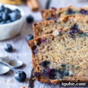 Moist Blueberry Banana Nut Bread 7 Three slices of blueberry banana bread on a wood table with fruit in the background.