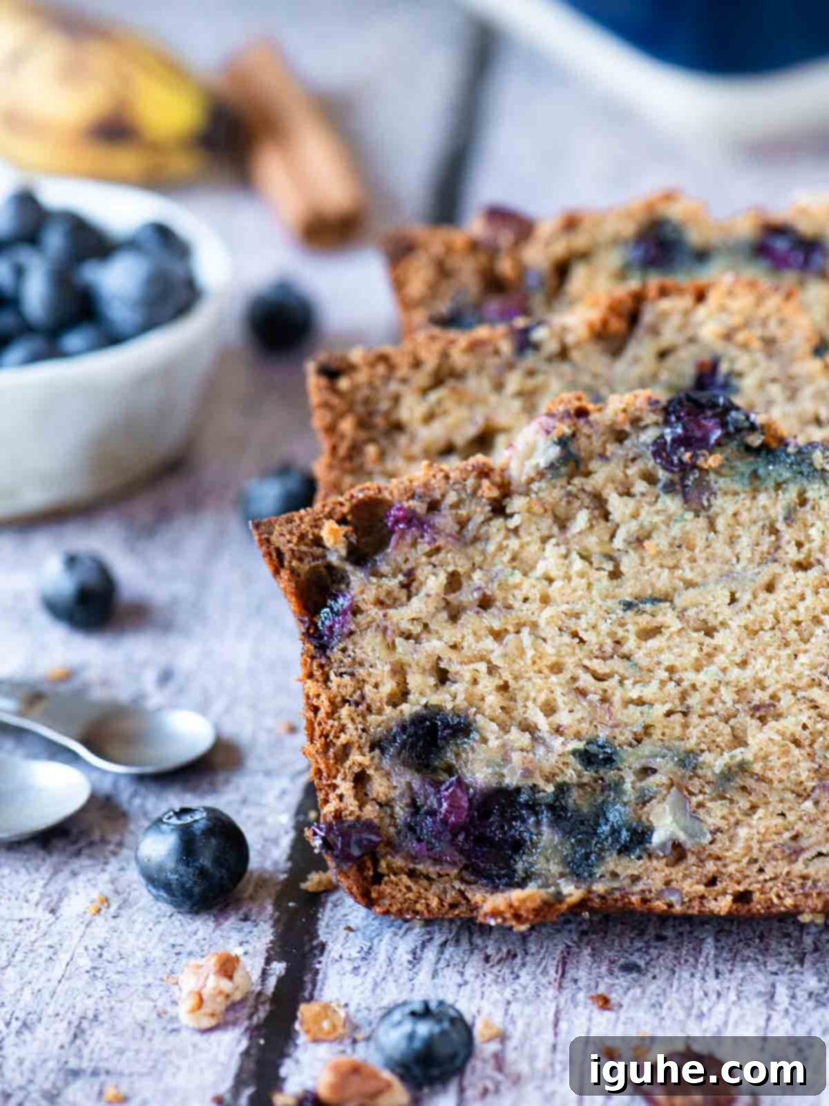 Moist Blueberry Banana Nut Bread 6 Three slices of blueberry banana bread on a wood table with fresh fruit in the background, ready to be served.