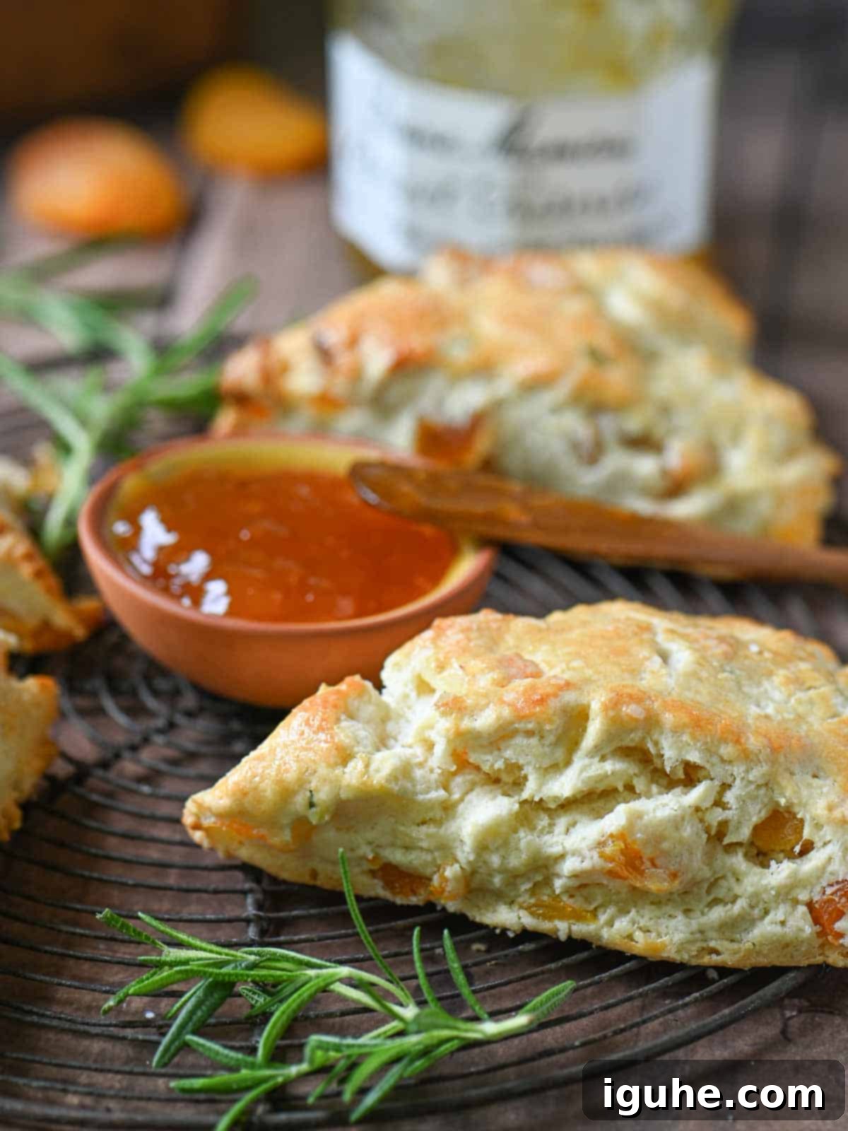 Sunshine Apricot Rosemary Scones 6 A close-up view of freshly baked scones, some with jam, resting on a wire rack.