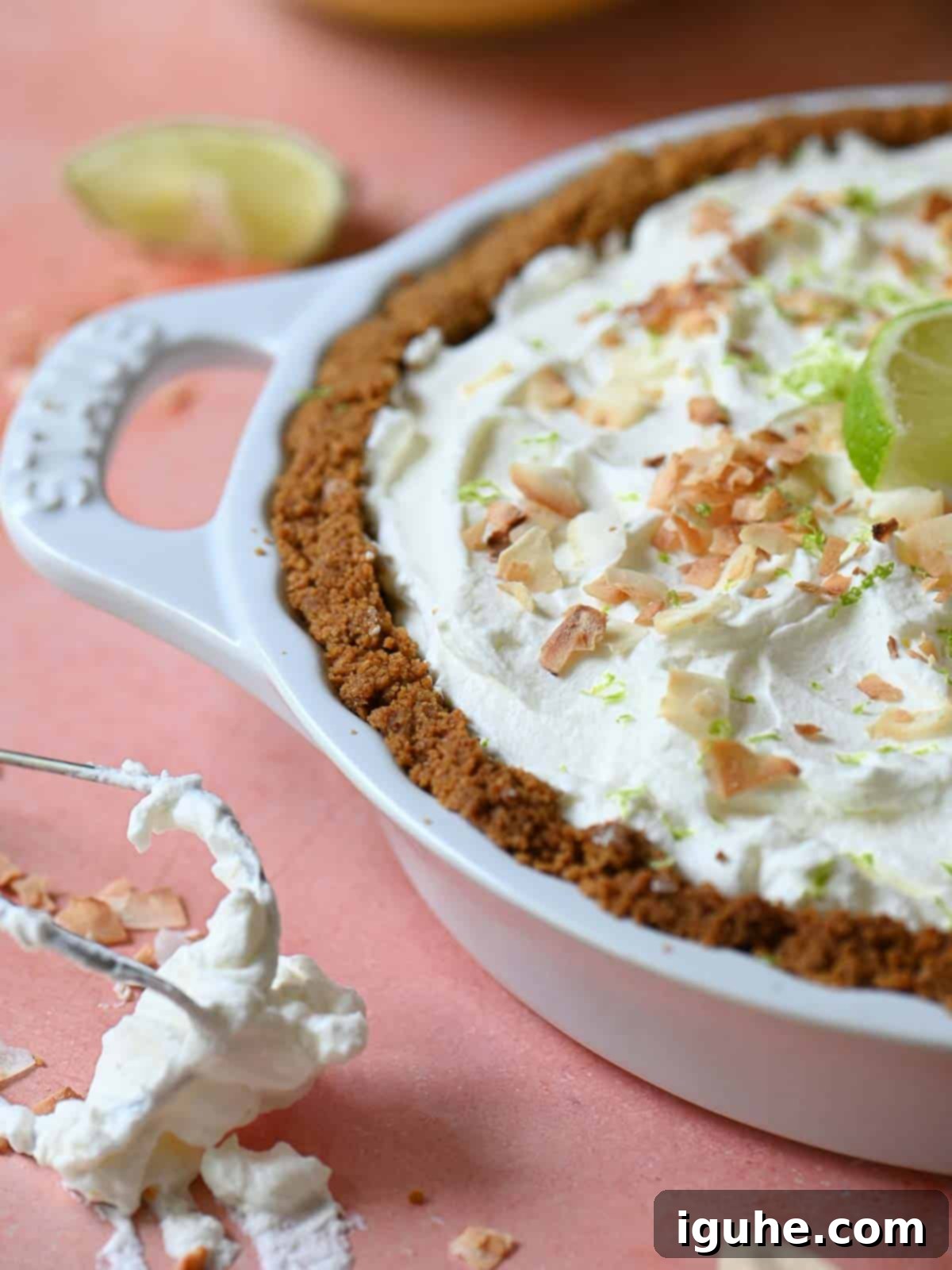 Close-up of coconut key lime pie on a pink surface with limes.