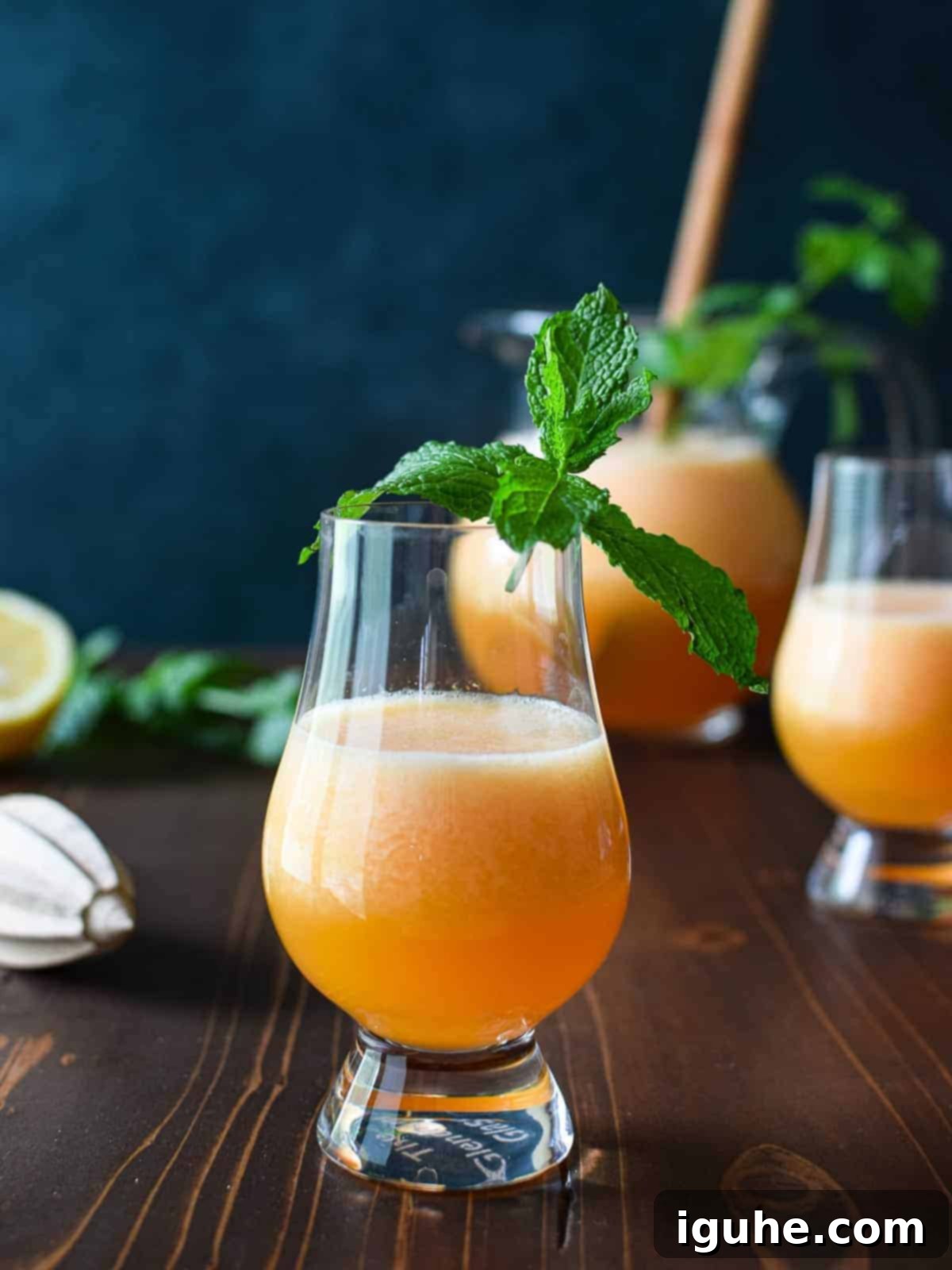 eye-level view of cantaloupe lime agua fresca in a clear glass on a brown table with mint and lime.