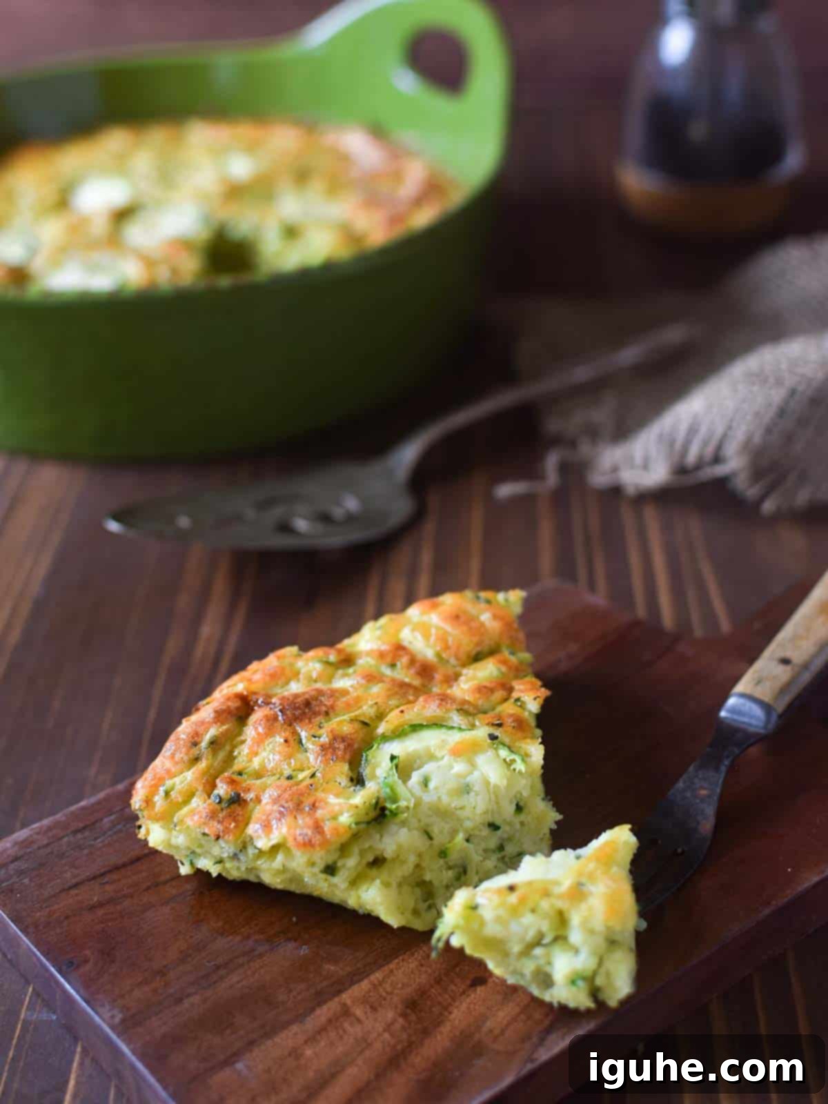 Naked Zucchini Quiche 2 A golden-brown slice of crustless zucchini pie with visible zucchini pieces, served on a wooden cutting board, ready to be enjoyed.