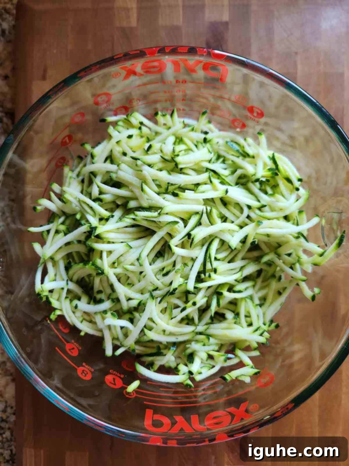 Naked Zucchini Quiche 4 Freshly shredded zucchini piled high in a clear glass bowl, ready to be combined with other ingredients for the pie.