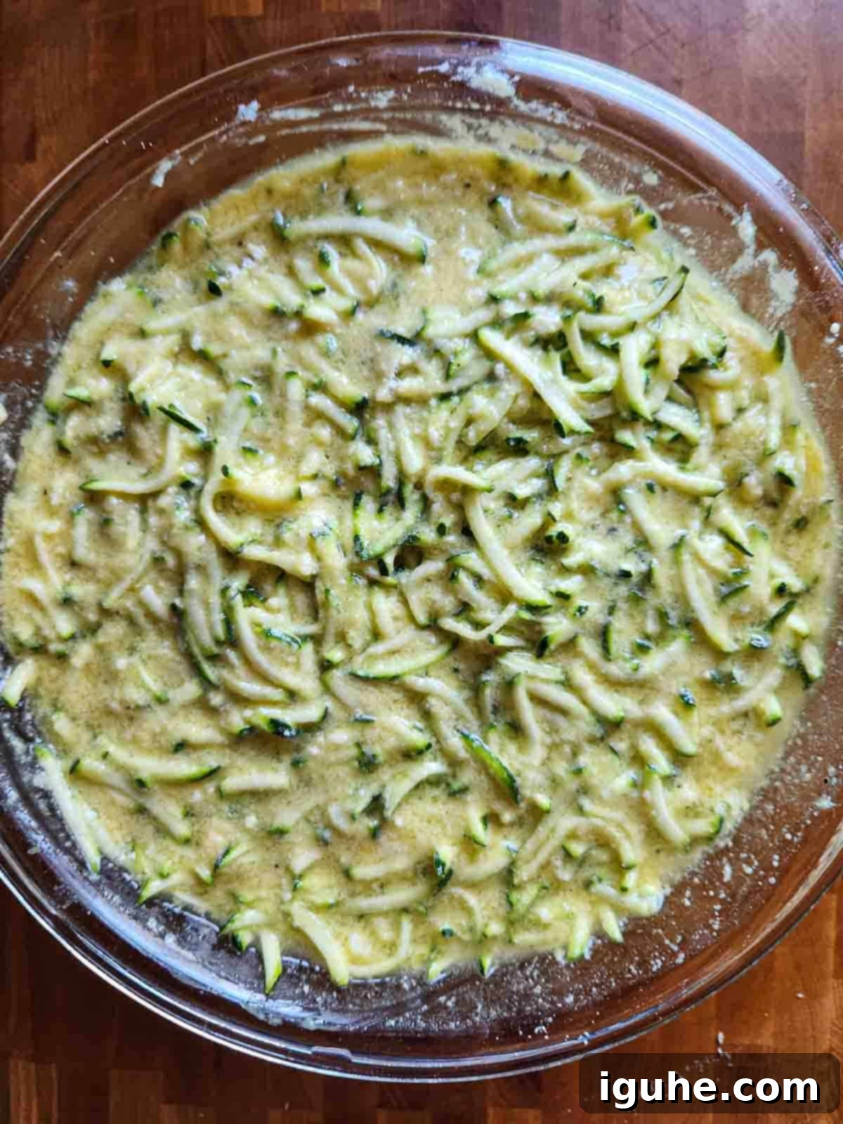 Savory Zucchini Bake 5 All ingredients for the zucchini pie, including shredded zucchini, eggs, Bisquick, and Parmesan, mixed together in a clear bowl to form a thick, uniform batter.