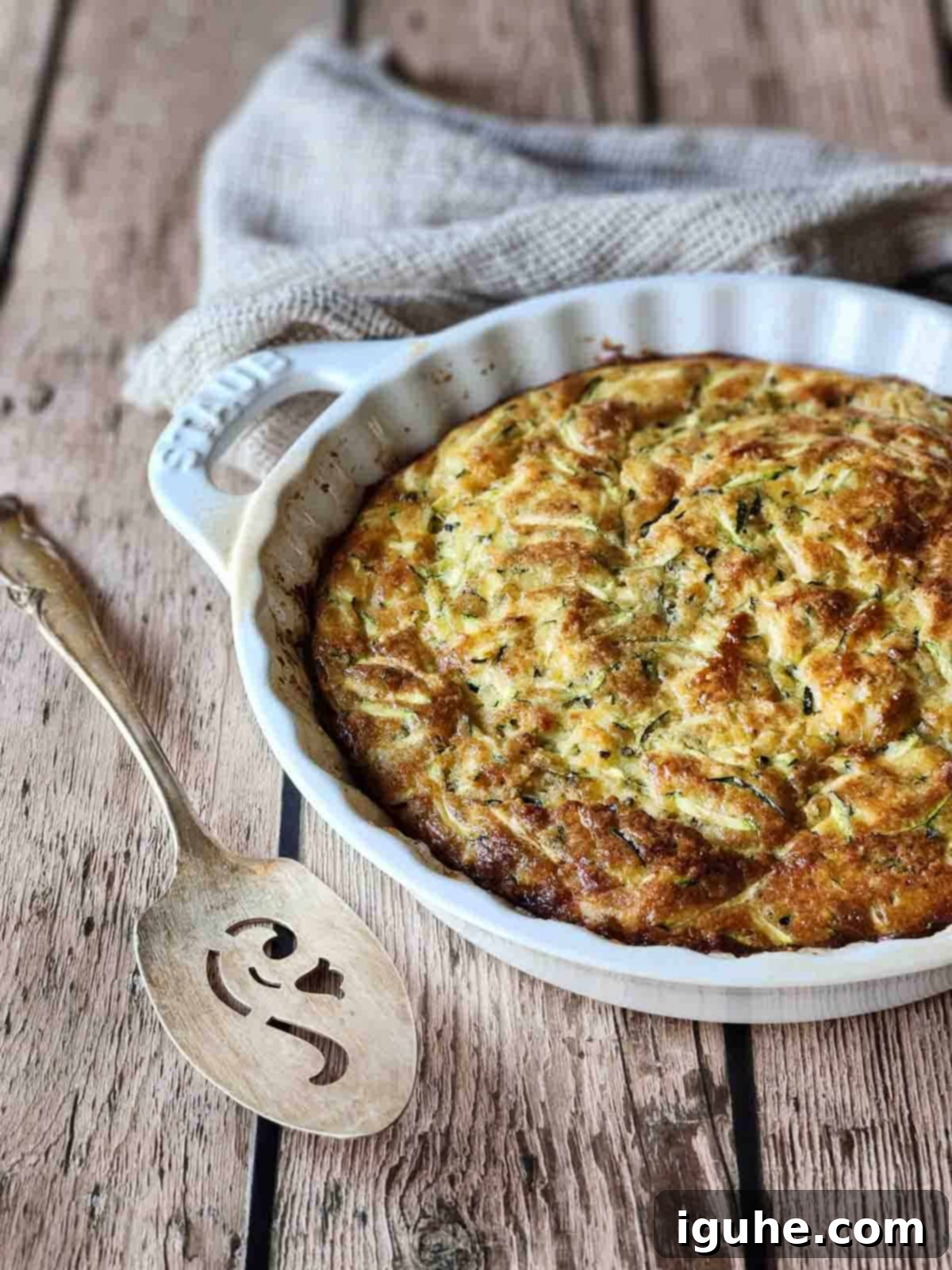 Naked Zucchini Quiche 7 A freshly baked, golden brown crustless zucchini pie, served in an elegant white ceramic dish, resting on a rustic wooden table, ready to be sliced.