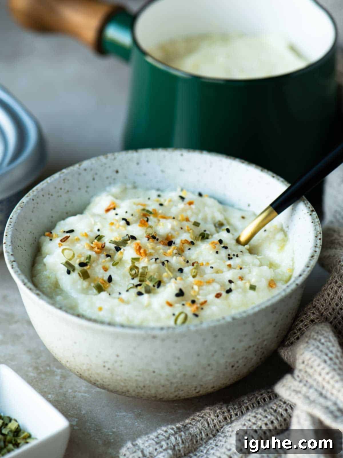 A steaming bowl of creamy grits with a spoon, ready to be enjoyed, with a rustic pot in the background.