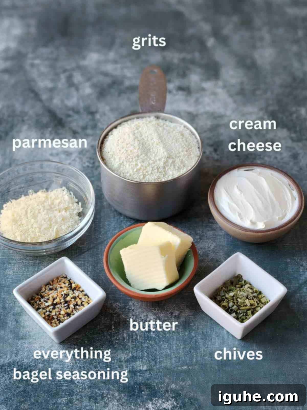 Creamy Everything Bagel Grits 3 An organized overview of all the fresh ingredients for making cream cheese grits laid out in bowls on a sleek grey surface.