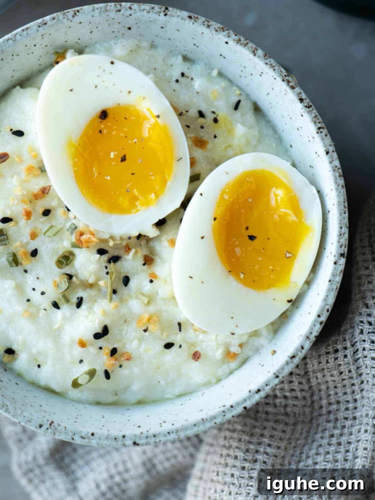 Creamy Everything Bagel Grits 6 Overhead of a bowl of grits with 2 jammy eggs split open on top, garnished with chives and everything bagel seasoning.