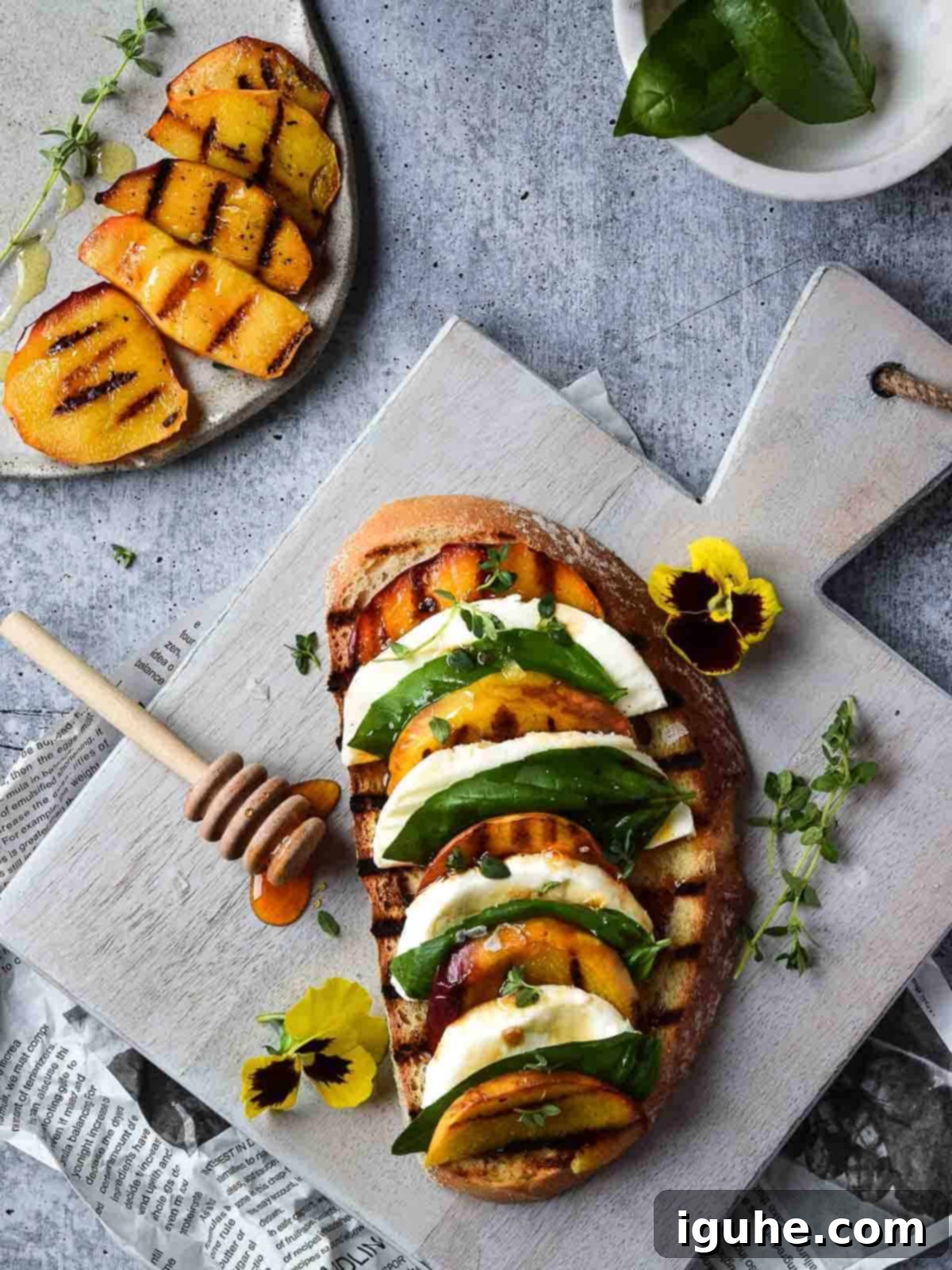 Overhead view of toast with grilled peaches on it layered with mozzerella, basil and balsamic vinegar on a grey cutting board