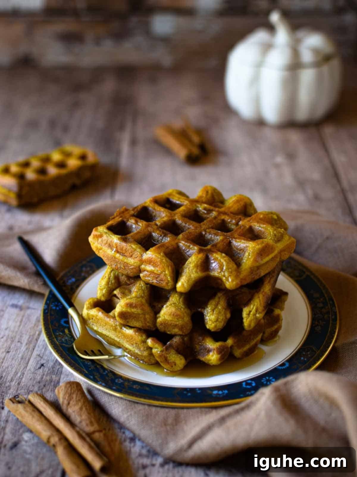 Pumpkin Spice Belgian Waffles 2 Stacked Belgian-style pumpkin spice waffles on a plate, generously drizzled with maple syrup and a sprinkle of cinnamon, set on a rustic wooden surface. Perfect for a cozy fall breakfast.
