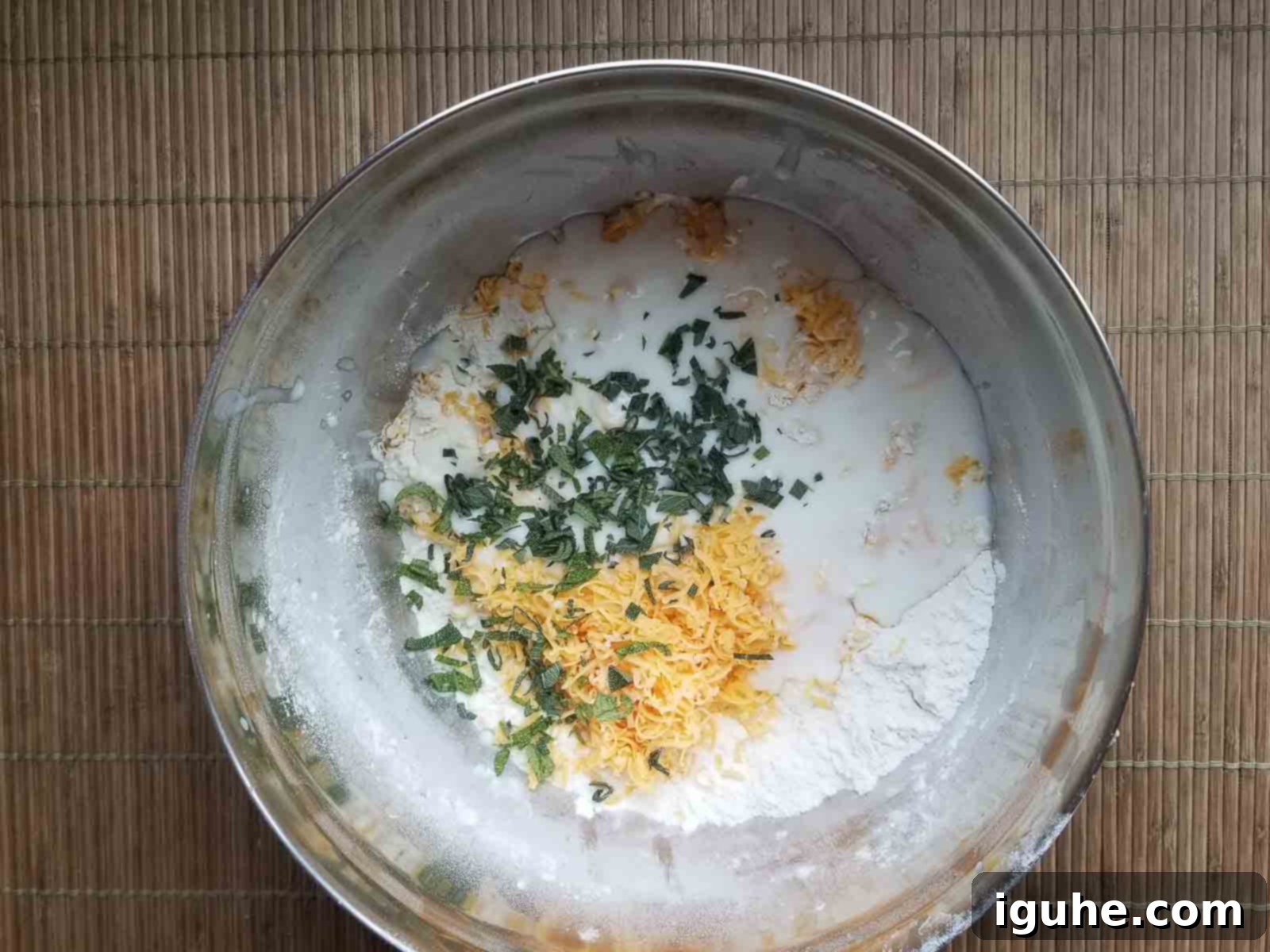 Golden Cheddar Sage Biscuits 6 Biscuit dough with buttermilk, grated cheddar cheese, and fresh sage mixed in a bowl, looking shaggy.